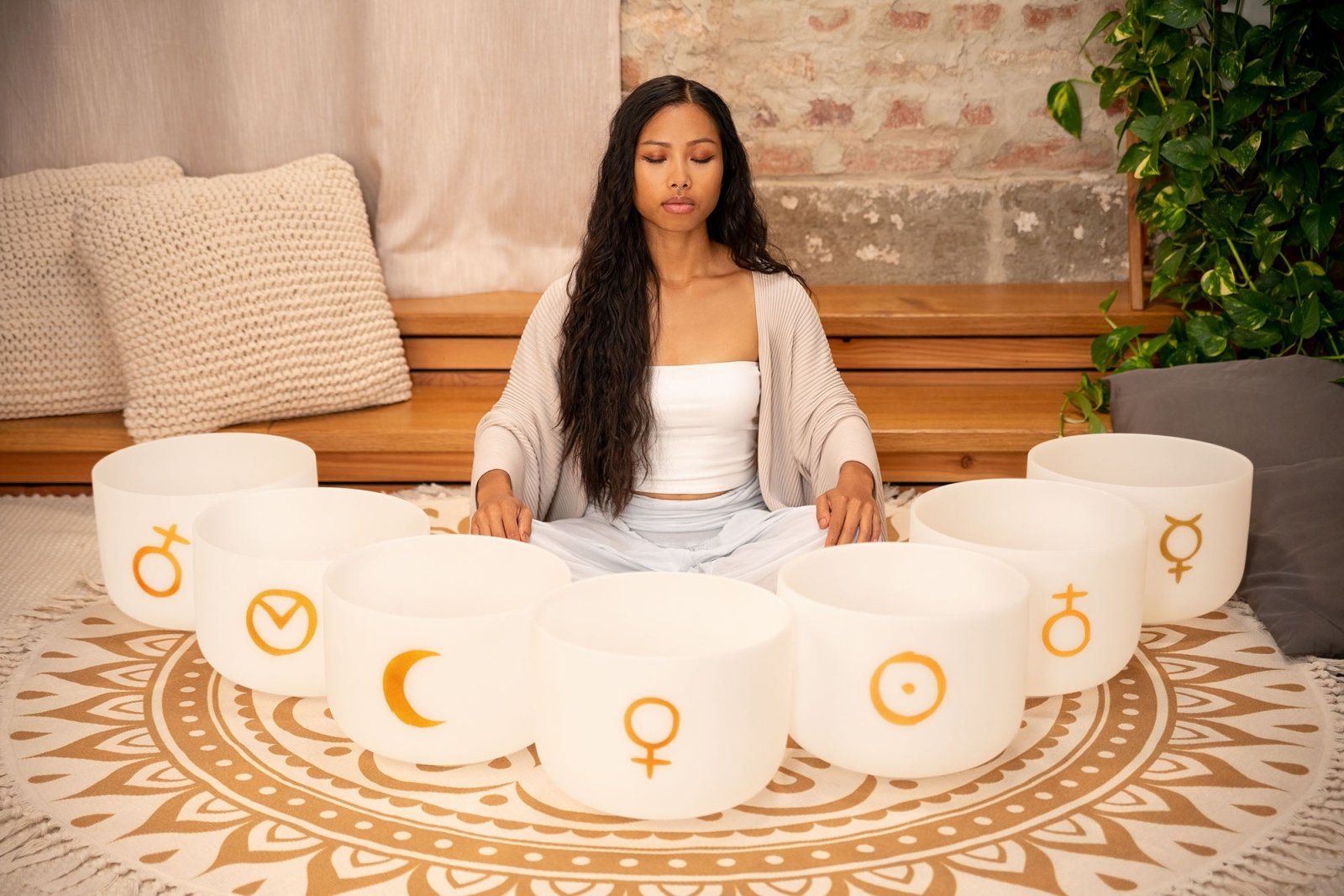 Woman seated in meditation posture surrounded by seven white frosted quartz crystal singing bowls with gold planetary symbols arranged in a circle — for Carpe Diem Dream