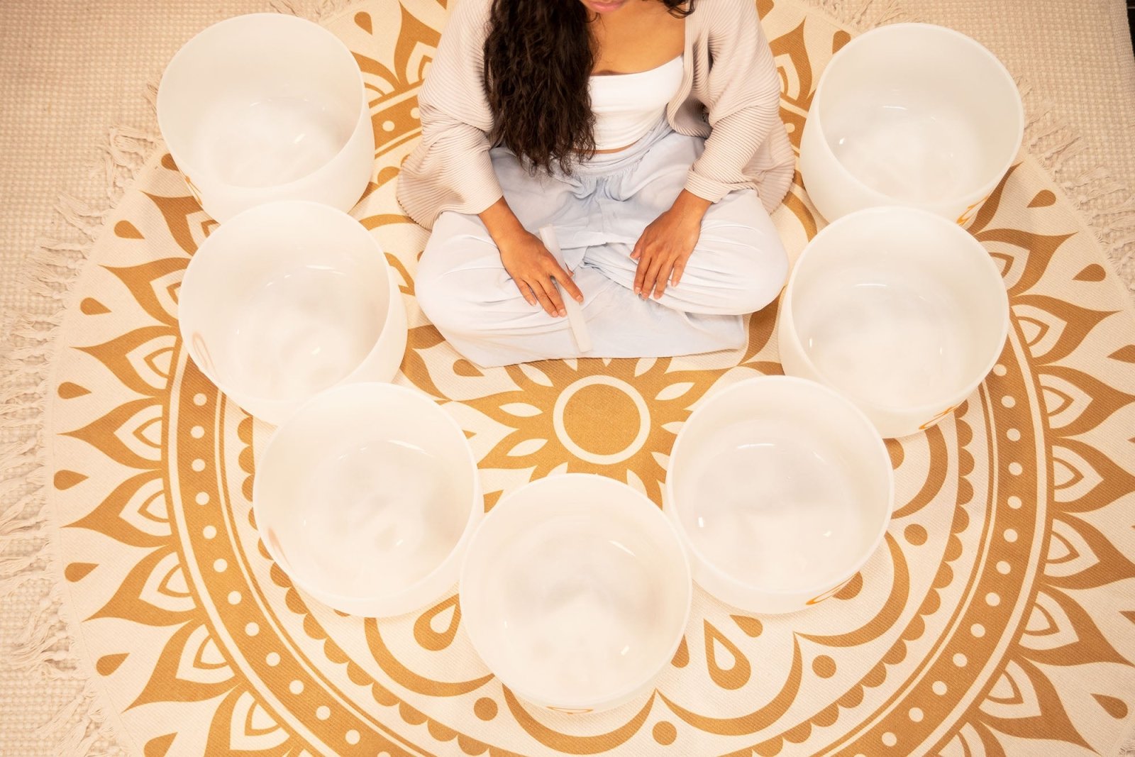 Top view of woman seated cross-legged with hands resting on her knees surrounded by seven white frosted quartz crystal singing bowls arranged in a circular formation — for Carpe Diem Dream
