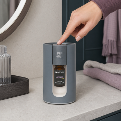 Portable waterless essential oil diffuser with a hand pressing the top control, showing the installed Lavender bottle on a pale stone counter with dark teal and mauve accents. — for Carpe Diem Dream