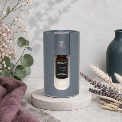 Portable waterless essential oil diffuser displayed on a pale stone pedestal with lavender, eucalyptus, blush botanicals, mauve textiles, and dark teal accents. — for Carpe Diem Dream