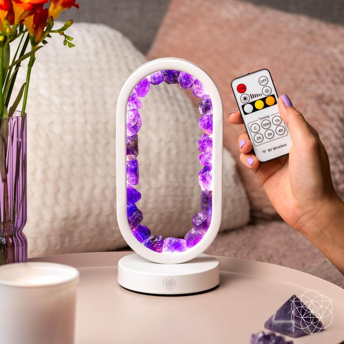 Decorative lamp with purple crystals and remote control in hand on a table surrounded by pillows and vase. Carpe Diem Dream