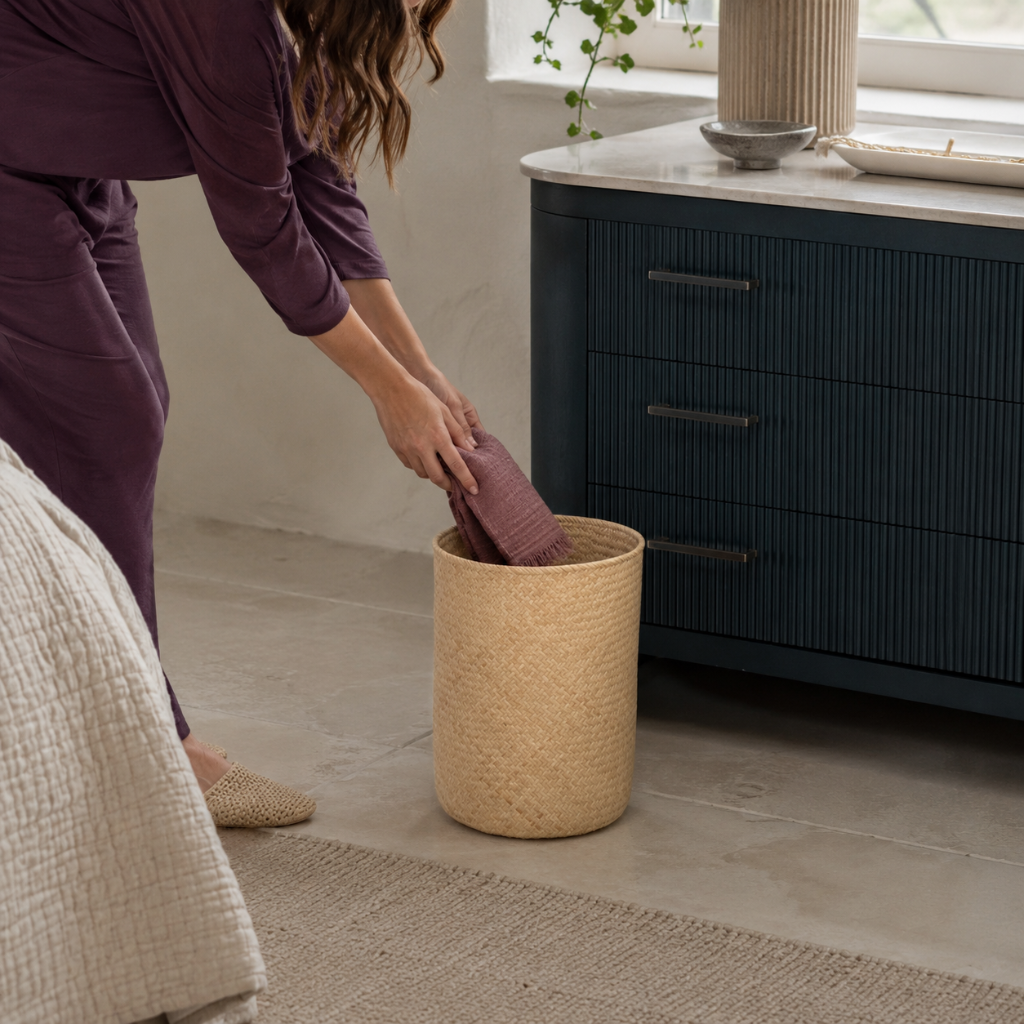 Praya handwoven rattan basket in natural woven finish shown in use as a mauve textile is placed inside beside dark teal cabinetry. — for Carpe Diem Dream