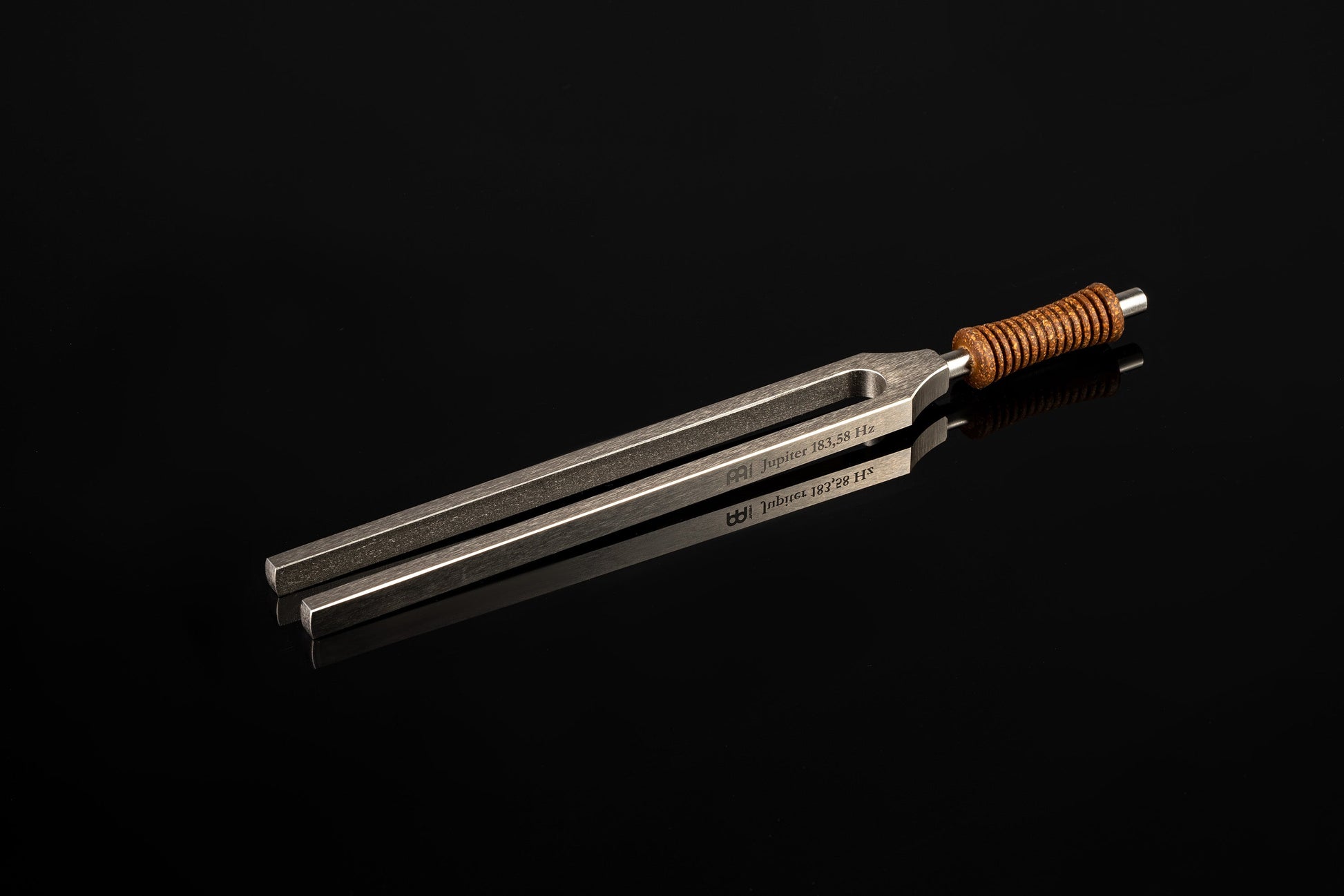 Weighted metal Jupiter tuning fork engraved 183.58 Hz with cork handle resting on a glossy black reflective surface. — for Carpe Diem Dream