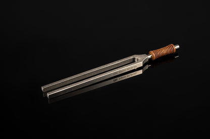 Weighted metal Jupiter tuning fork engraved 183.58 Hz with cork handle resting on a glossy black reflective surface. — for Carpe Diem Dream