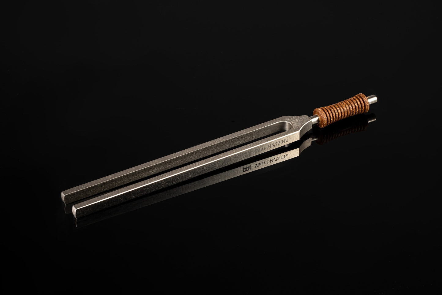 Weighted metal Mars tuning fork engraved 144.72 Hz with cork handle resting on a glossy black reflective surface. — for Carpe Diem Dream
