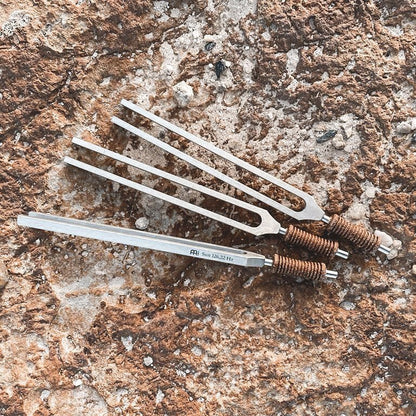 Several weighted metal tuning forks with cork handles arranged on a textured stone surface. — for Carpe Diem Dream