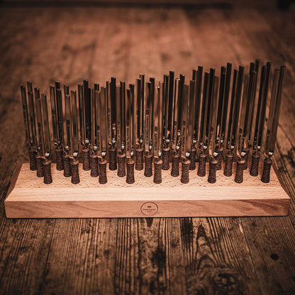 Twenty-seven planetary tuned metal tuning forks arranged in a beech wood holder on a rustic wooden surface in warm ambient lighting. — for Carpe Diem Dream
