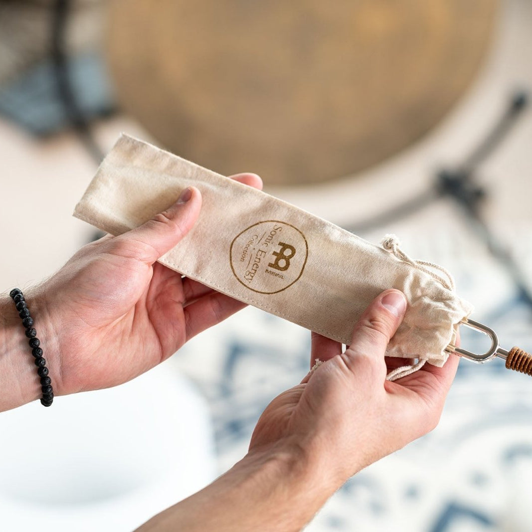 Hands holding a planetary tuned tuning fork inside its natural cotton storage pouch with engraved logo detailing. — for Carpe Diem Dream