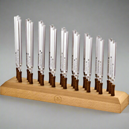 Twenty-seven weighted planetary therapy tuning forks standing upright in a wooden holder against a light neutral background. — for Carpe Diem Dream