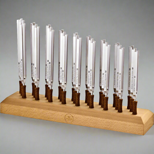 Twenty-seven weighted planetary therapy tuning forks standing upright in a wooden holder against a light neutral background. — for Carpe Diem Dream