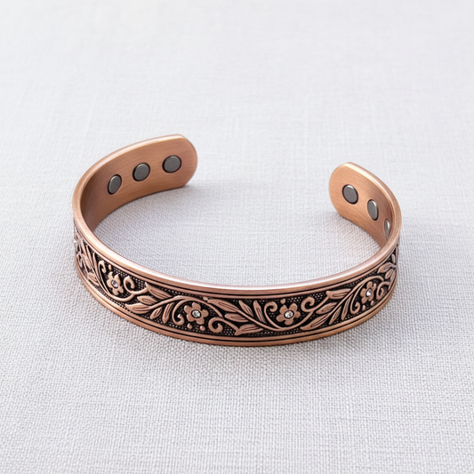 A pure copper floral cuff bracelet with leaf detailing and magnetic elements displayed upright on a soft neutral textured background. — for Carpe Diem Dream
