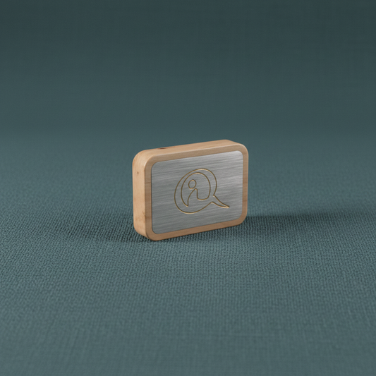 A compact Qi-Me EMF protection device with a brushed metal face and wood frame displayed on a muted teal linen surface with soft diffused lighting. — for Carpe Diem Dream