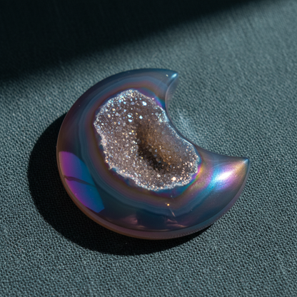 A rainbow agate druzy moon crystal with a sparkling druzy center displayed on a muted teal linen surface with soft directional lighting. — for Carpe Diem Dream