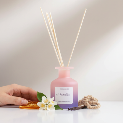 A frosted glass reed diffuser in a pink to purple gradient shown beside a hand with citrus slices, white flowers, and natural elements for size reference on a soft neutral surface. — for Carpe Diem Dream