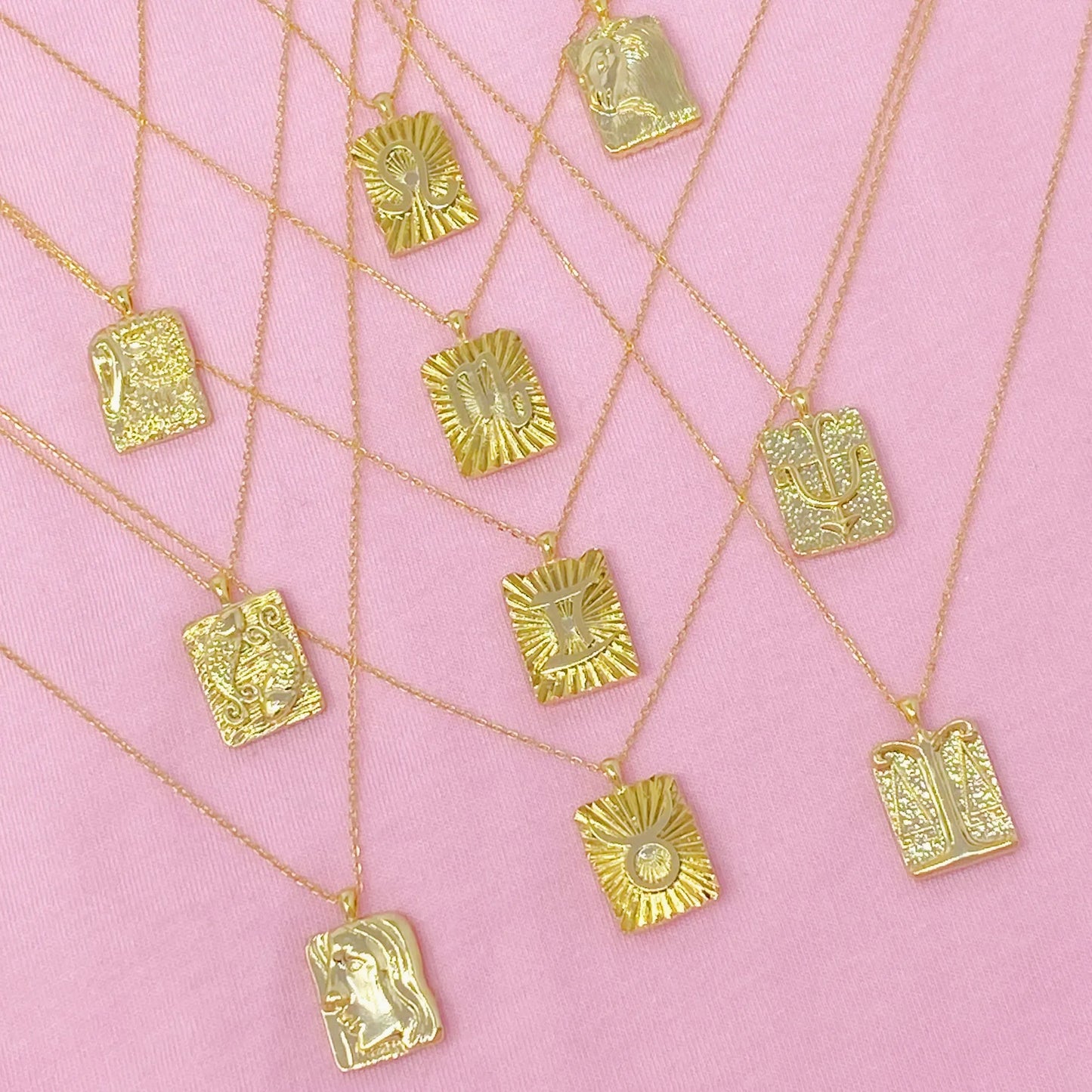 Reversible gold zodiac necklaces with constellation pendant, showing both polished and engraved sides on pink background for Carpe Diem Dream
