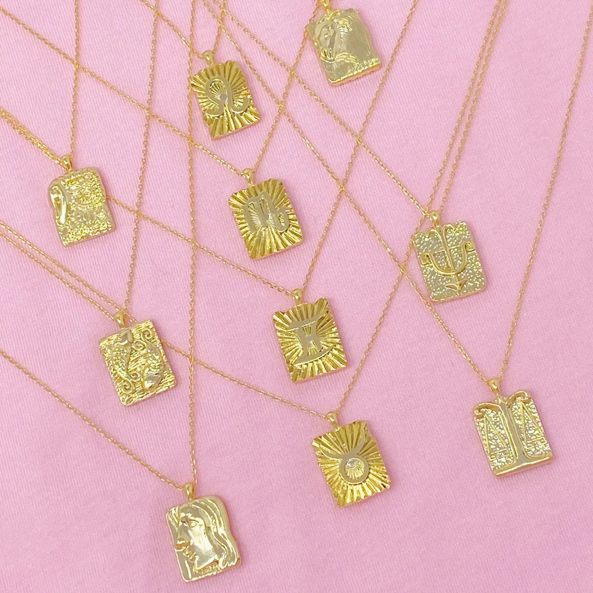 Reversible gold zodiac necklaces with constellation pendant, showing both polished and engraved sides on pink background for Carpe Diem Dream