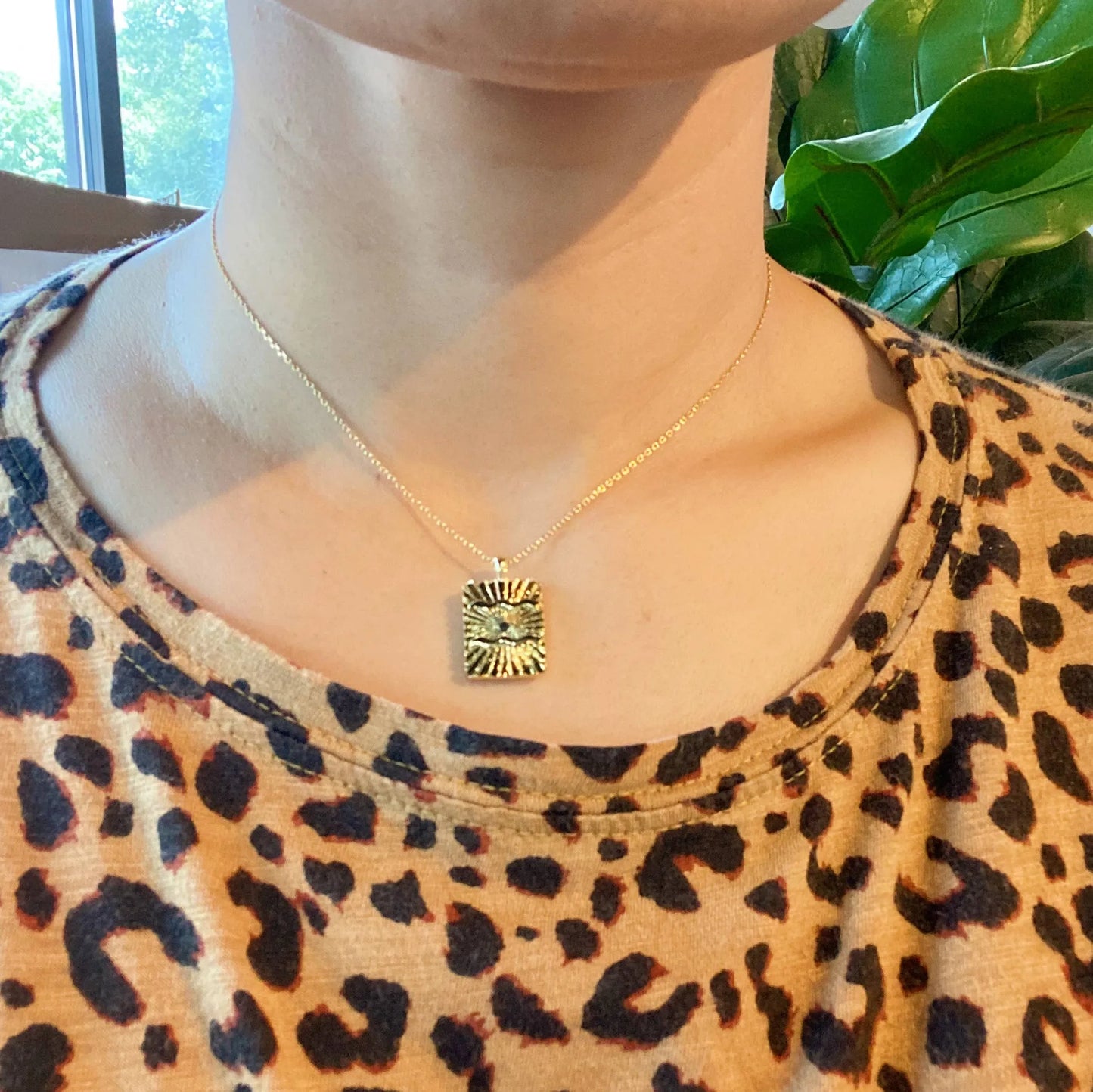 Reversible gold zodiac necklace with constellation pendant, showing both polished and engraved sides on person with leopard shirt background.