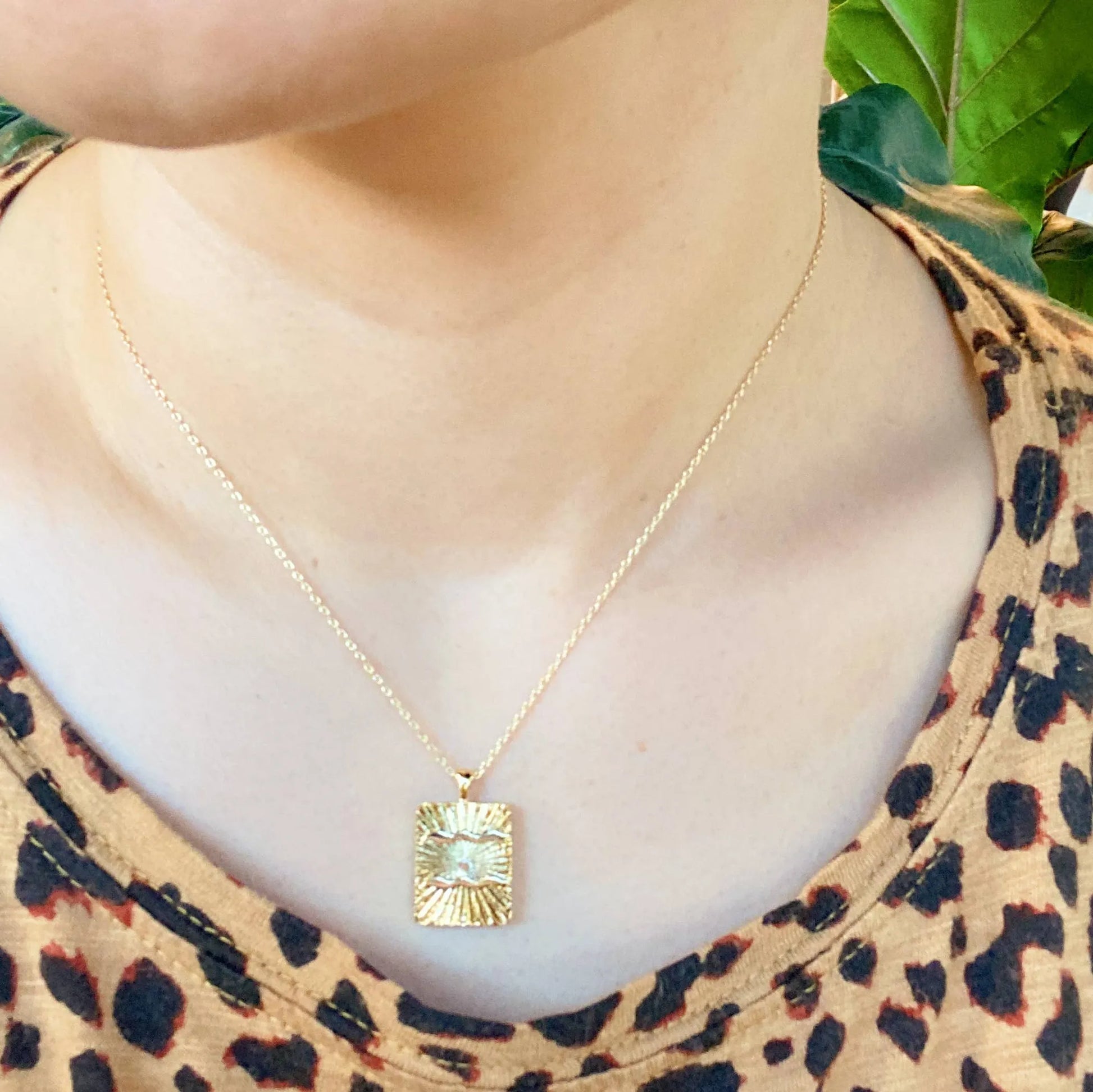 Reversible gold zodiac necklace with constellation pendant, showing both polished and engraved sides worn on person with leopard shirt background.
