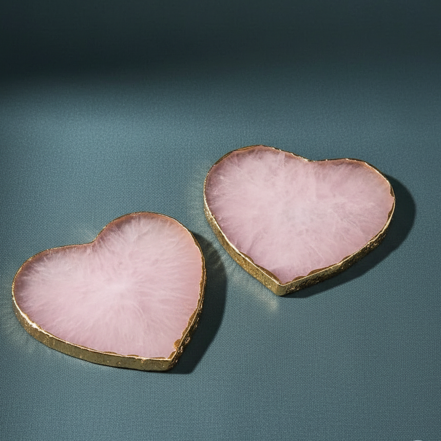 Two heart-shaped rose quartz coasters with gold edging displayed on soft teal surface. — for Carpe Diem Dream