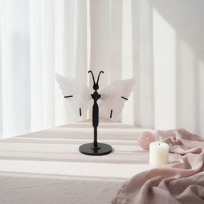 Rose quartz crystal butterfly wings on a black stand styled on a linen-covered table with soft window light, a candle, and a rose quartz sphere in a calm home setting. — for Carpe Diem Dream