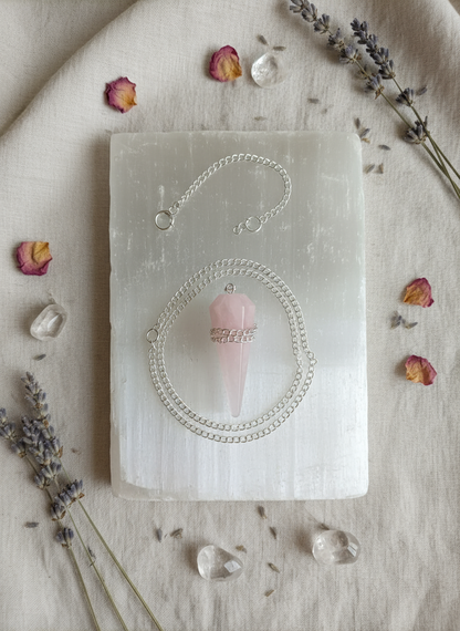 Rose Quartz crystal pendulum resting on a selenite slab surrounded by dried lavender, rose petals, and natural light on a linen surface – for Carpe Diem Dream.