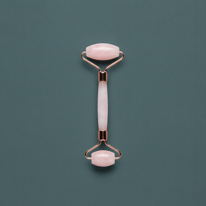 A dual-ended rose quartz facial roller with polished crystal rollers and rose gold frame displayed upright on a muted sage textured background. — for Carpe Diem Dream