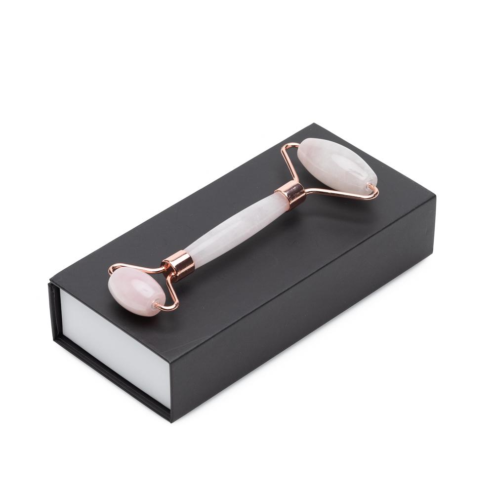 A dual-ended rose quartz facial roller with rose gold frame resting on top of a closed black presentation gift box. — for Carpe Diem Dream