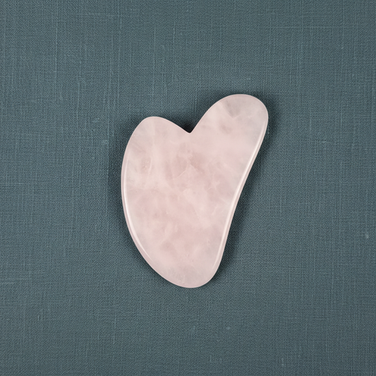A rose quartz gua sha facial tool displayed on a muted teal linen background with soft lighting. — for Carpe Diem Dream