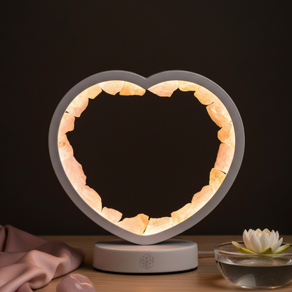 A heart-shaped rose quartz lamp glowing softly on a wooden surface beside a blush satin cloth, lotus bowl, and smooth stones in warm ambient light. — for Carpe Diem Dream