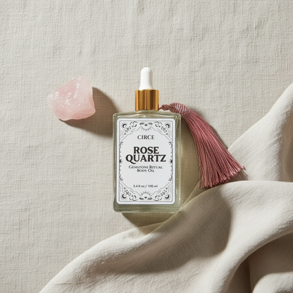 Rose Quartz Ritual Body Oil glass dropper bottle with pink tassel displayed on linen fabric beside a rose quartz crystal. — for Carpe Diem Dream