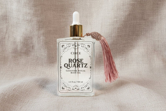 Rose Quartz Ritual Body Oil glass dropper bottle with pink tassel displayed on a soft linen background. — for Carpe Diem Dream