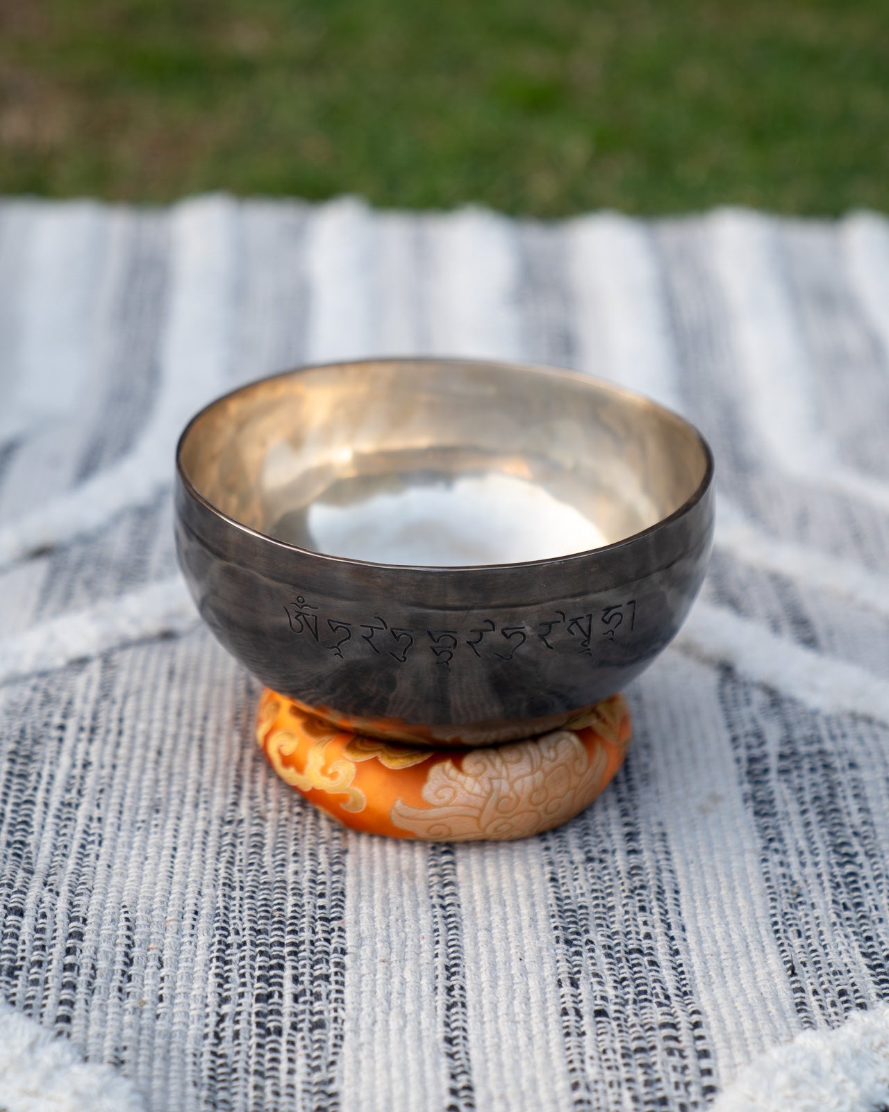 Back view of a Sacral Chakra New Moon singing bowl showing engraved Tibetan mantra resting on an orange cushion. — for Carpe Diem Dream