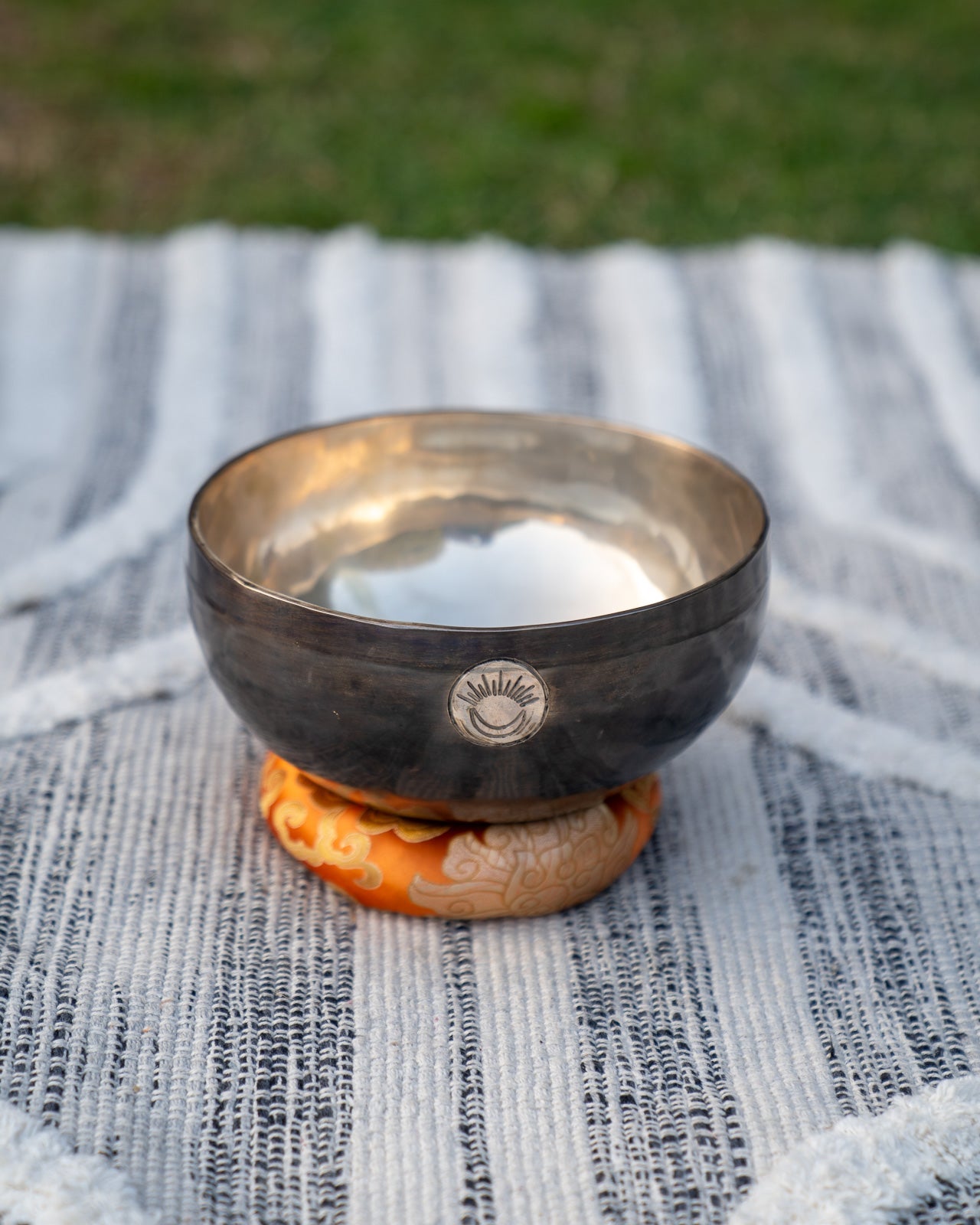Front view of a Sacral Chakra New Moon singing bowl with engraved sun and moon symbol resting on an orange cushion. — for Carpe Diem Dream