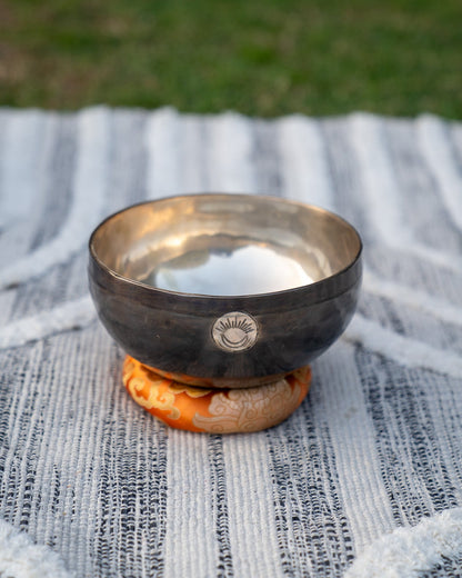Front view of a Sacral Chakra New Moon singing bowl with engraved sun and moon symbol resting on an orange cushion. — for Carpe Diem Dream