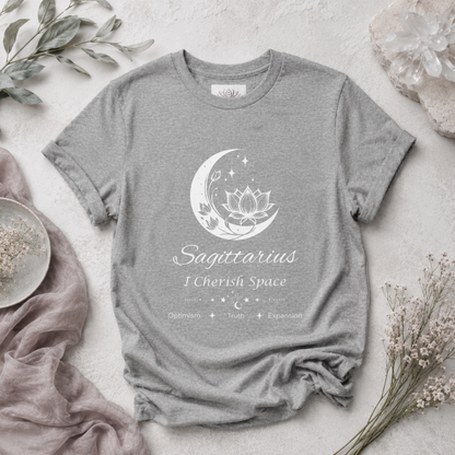 Sagittarius Moon I Cherish Space zodiac T-shirt in Athletic Heather with white moon-inspired lotus, floral, and celestial artwork and Optimism, Truth, Expansion text, styled in a cool-toned studio botanical flat lay. — for Carpe Diem Dream