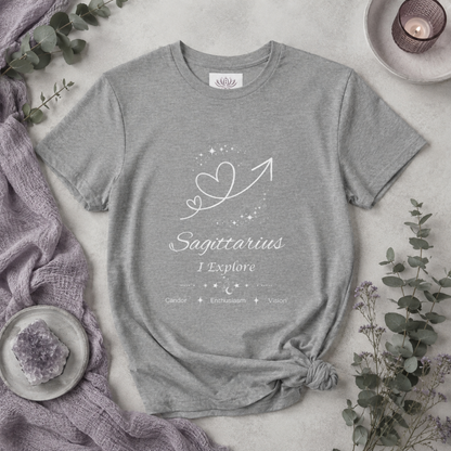 Sagittarius Rising I Explore zodiac T-shirt in Athletic Heather with white celestial heart and arrow artwork and Candor, Enthusiasm, Vision text, styled in a cool-toned studio botanical flat lay. — for Carpe Diem Dream