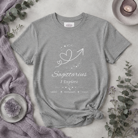 Sagittarius Rising I Explore zodiac T-shirt in Athletic Heather with white celestial heart and arrow artwork and Candor, Enthusiasm, Vision text, styled in a cool-toned studio botanical flat lay. — for Carpe Diem Dream