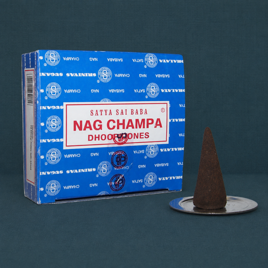Satya Nag Champa dhoop cones box with one brown cone on a small metal disc burner against a dark teal textured linen background. — for Carpe Diem Dream
