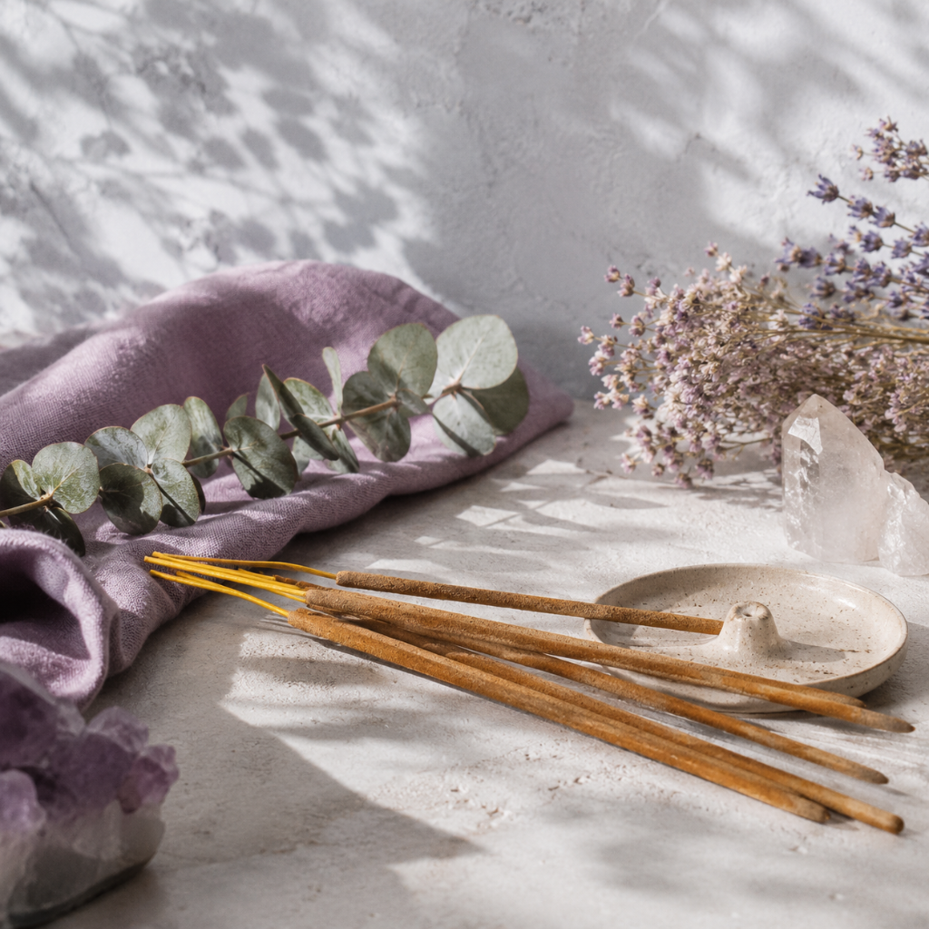 Close-up of Satya Nag Champa incense sticks and a ceramic incense holder styled with eucalyptus, lavender, mauve textile, and crystals. — for Carpe Diem Dream.