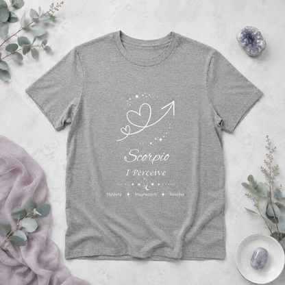 Scorpio Rising I Perceive zodiac T-shirt in Athletic Heather with white celestial heart and arrow artwork and Mystery, Magnetism, Resolve text, styled in a cool-toned studio botanical flat lay. — for Carpe Diem Dream