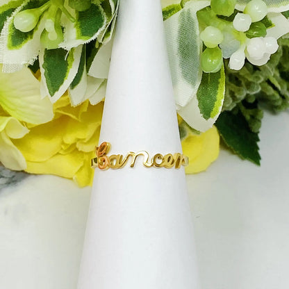 18K gold Scripted Zodiac Ring featuring delicate cursive lettering of zodiac Cancer, displayed on white botanical background for Carpe Diem Dream