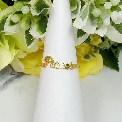 18K gold Scripted Zodiac Ring featuring delicate cursive lettering of zodiac Pisces, displayed on white botanical background for Carpe Diem Dream