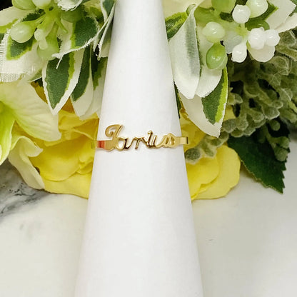 18K gold Scripted Zodiac Ring featuring delicate cursive lettering of zodiac Taurus, displayed on white botanical background for Carpe Diem Dream.