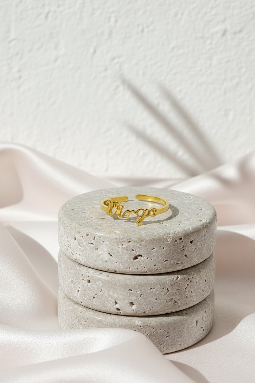 18K gold Scripted Zodiac Ring featuring delicate cursive lettering of zodiac Virgo, displayed on travertine and pink silk botanical shadow background for Carpe Diem Dream.