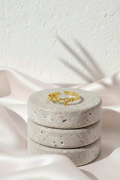 18K gold Scripted Zodiac Ring featuring delicate cursive lettering of zodiac Virgo, displayed on travertine and pink silk botanical shadow background for Carpe Diem Dream.