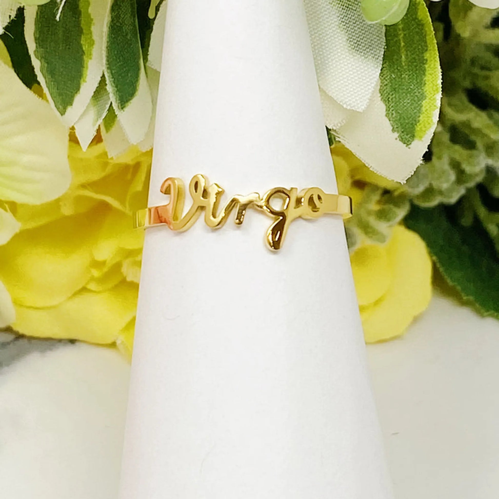 18K gold Scripted Zodiac Ring featuring delicate cursive lettering of zodiac Virgo, displayed on white botanical background for Carpe Diem Dream
