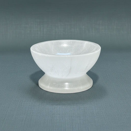 A translucent white selenite crystal bowl with pedestal displayed upright on a muted sage linen background. — for Carpe Diem Dream