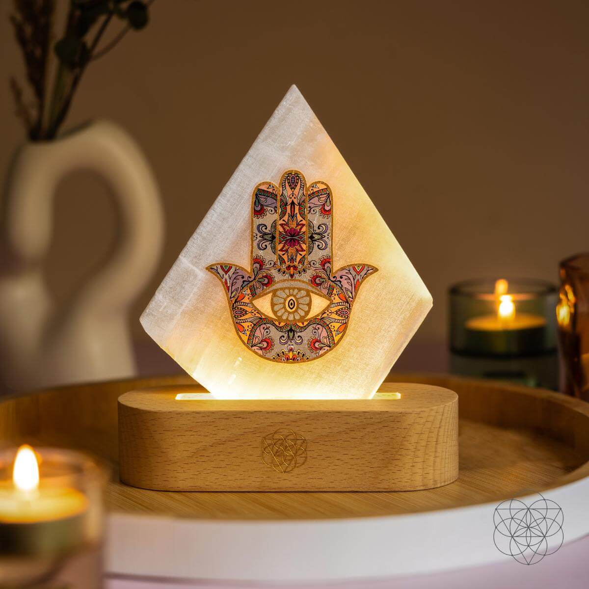 Selenite Mood Lamp with ornate Hamsa Hand design illuminated in warm golden light, resting on a wooden base beside candles and soft neutral decor — styled by Carpe Diem Dream.