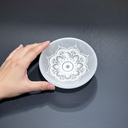 A translucent white selenite mandala lotus bowl shown beside a hand to illustrate its size and engraved design on a dark textured surface. — for Carpe Diem Dream
