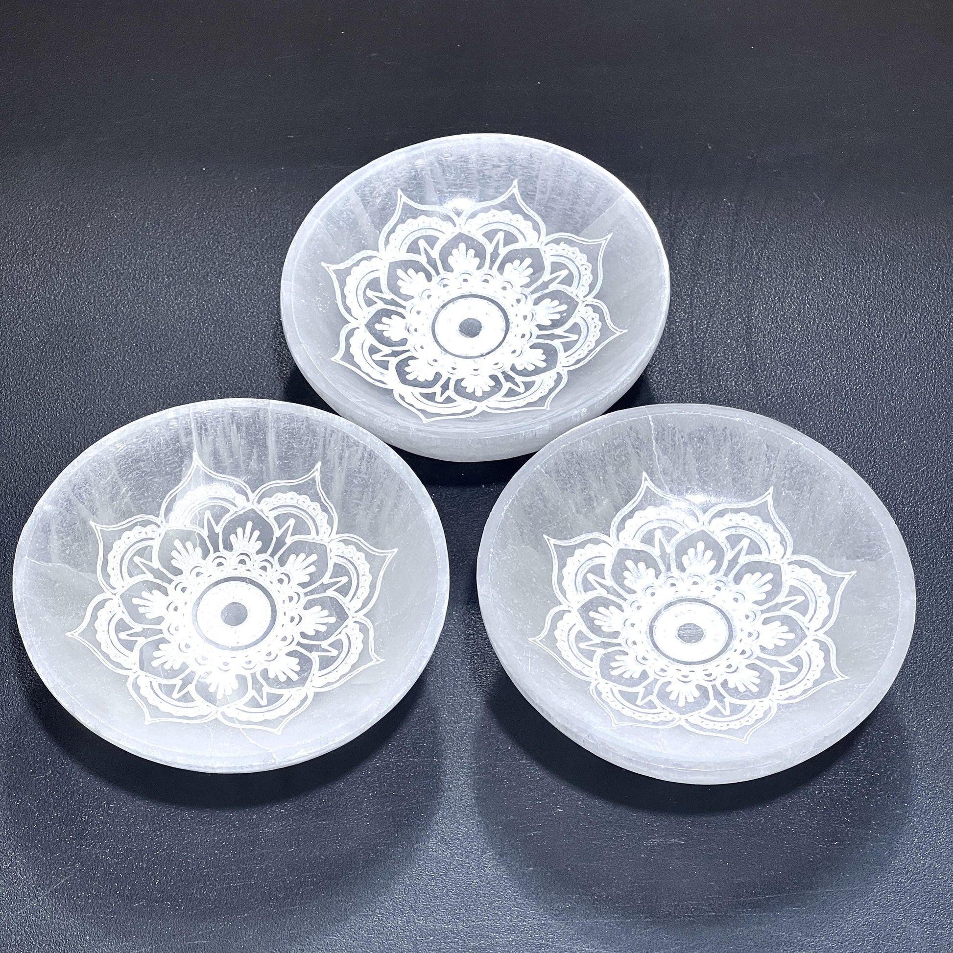 Three translucent white selenite mandala lotus bowls arranged together on a dark textured surface. — for Carpe Diem Dream